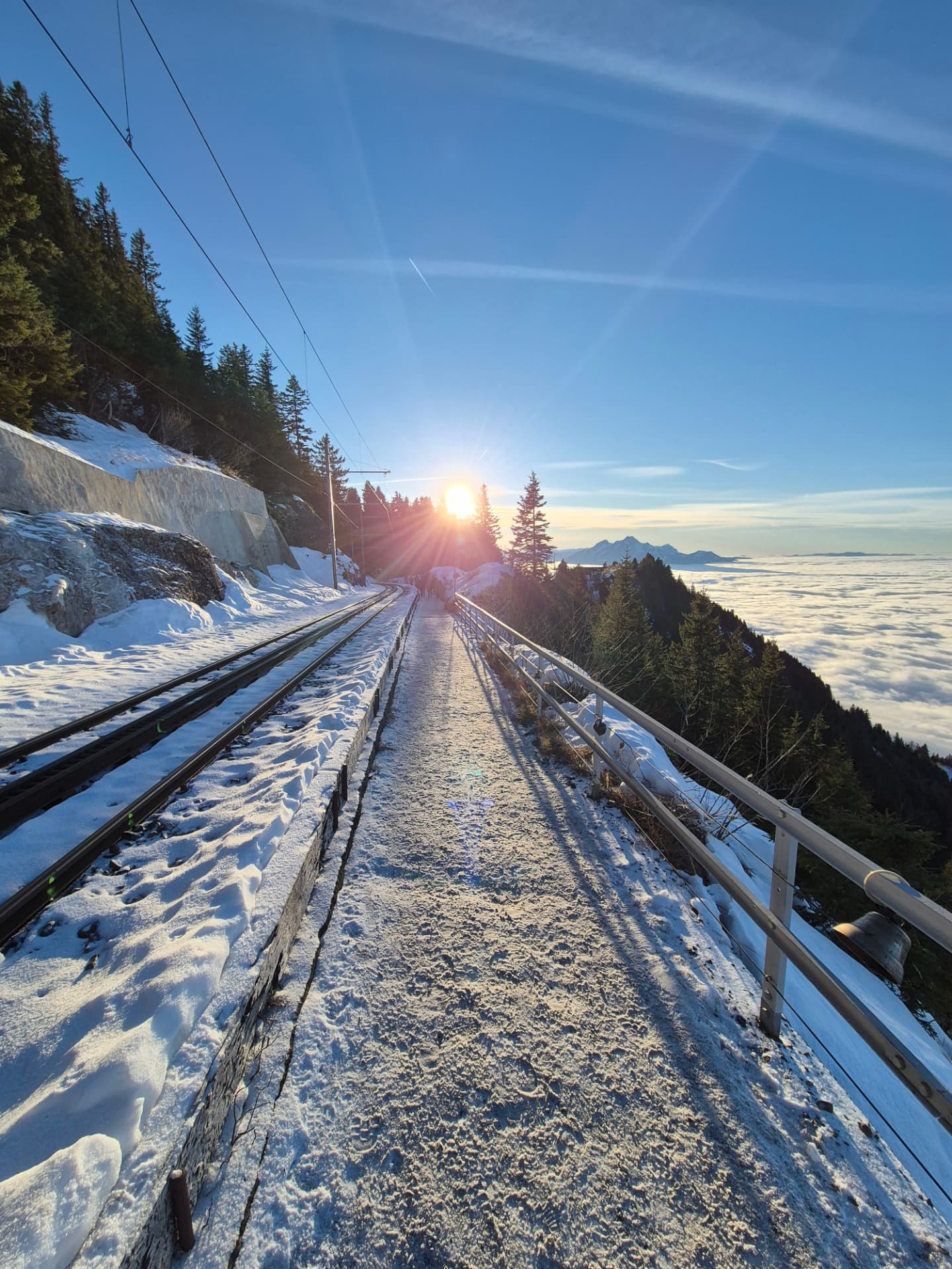 Schneebedeckter Weg entlang einer Bergbahn im Gegenlicht der Abendsonne