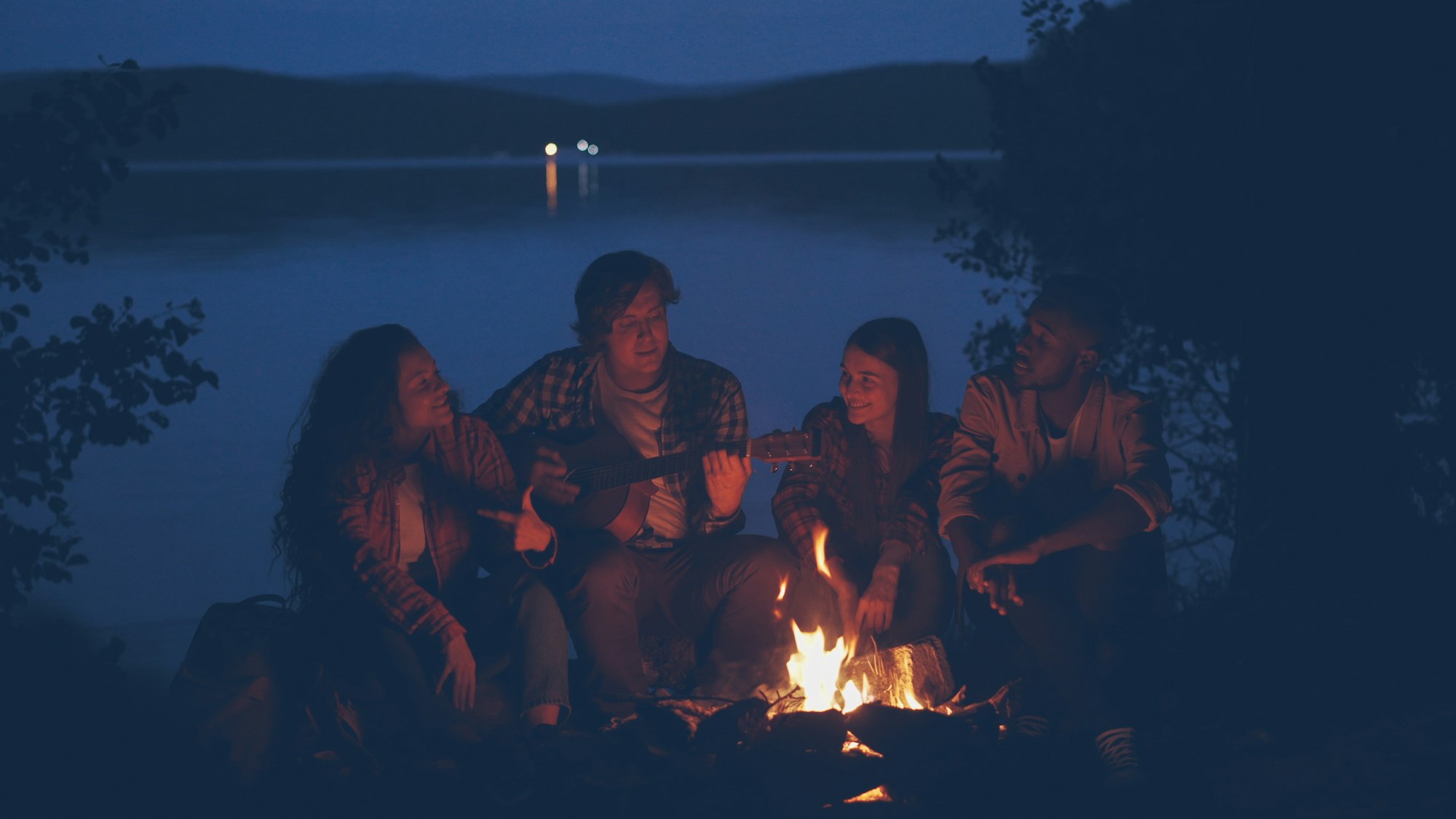 Menschen sitzen gemeinsam am Lagerfeuer am See in der Abenddämmerung